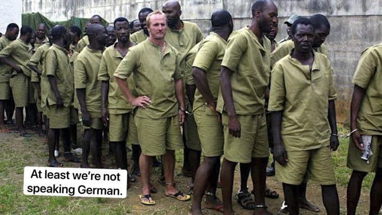 Une photo d'hommes faisant la queue, portant tous le même uniforme composé d'un short vert et d'une chemise verte. L'un des hommes est blanc, tous les autres sont noirs. Le texte en bas à gauche indique "Au moins, nous ne parlons pas allemand".