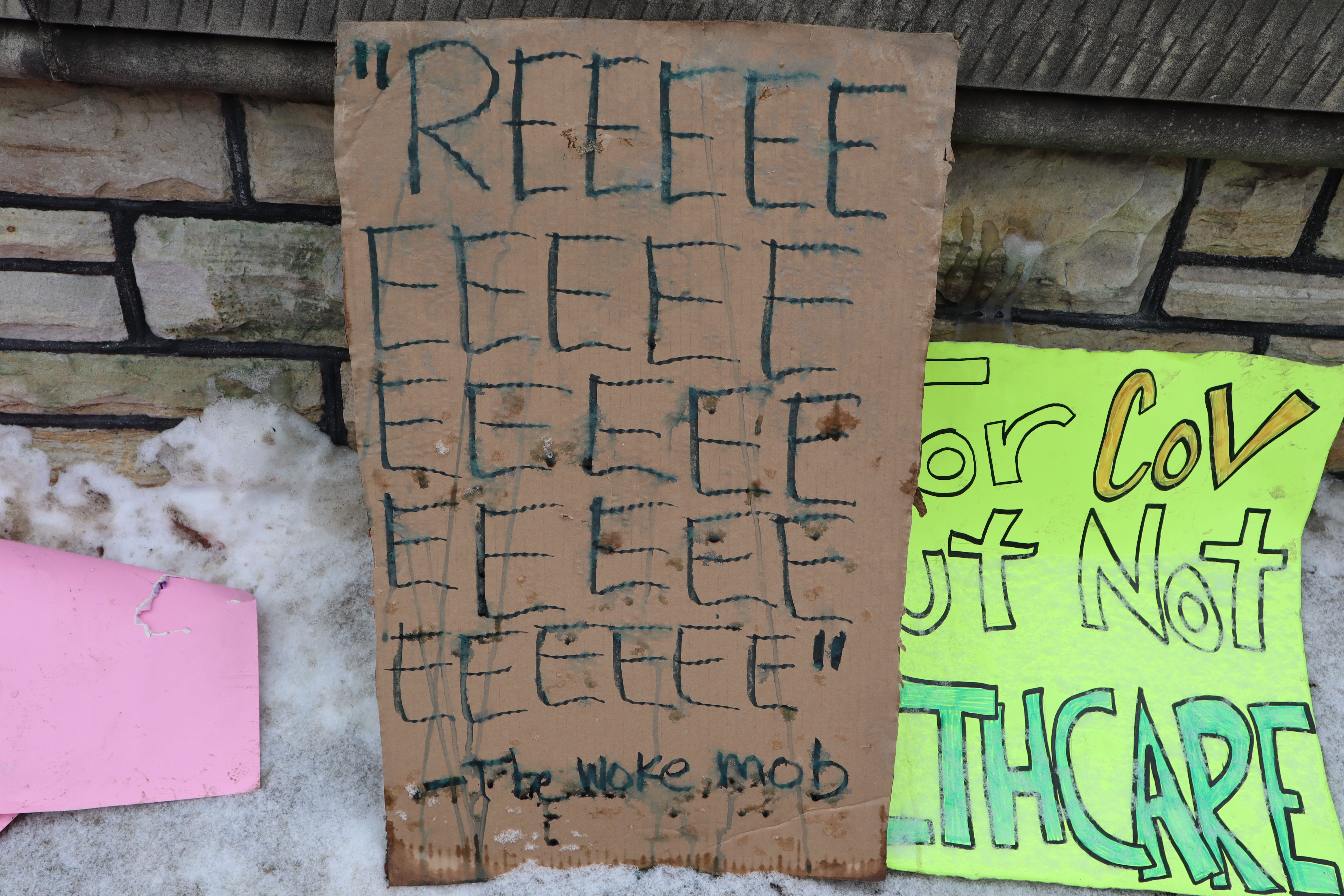 Un carton placé sur une clôture en pierre dans la neige. Il lit "REEEEE .. [21 autres 'E's] - The Woke mob [sic]".