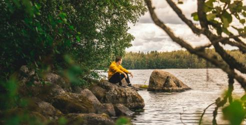 En man i gul jakke sitter på en stein og ser ut over en innsjø.