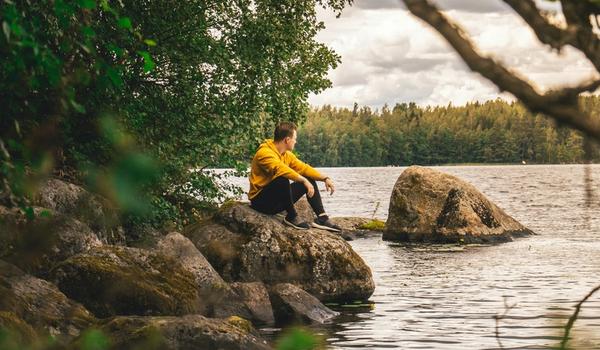 En man i gul jakke sitter på en stein og ser ut over en innsjø.