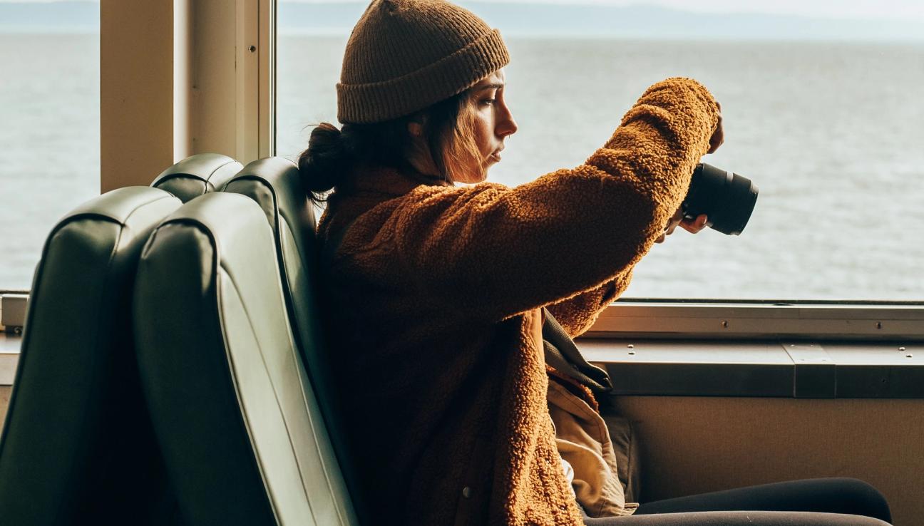 Jente sitter på tog og holder et kamera. bilde.