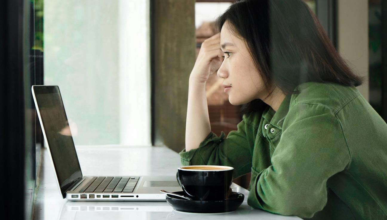 Nainen katsoo kannettavaa tietokonettaan ja lukee tietoja henkilöllisyyden suojauspalvelustaan. Valokuva.