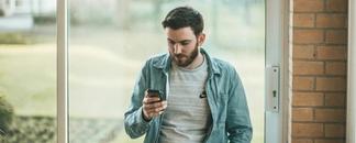 Man med mobil i handen står vid fönstret