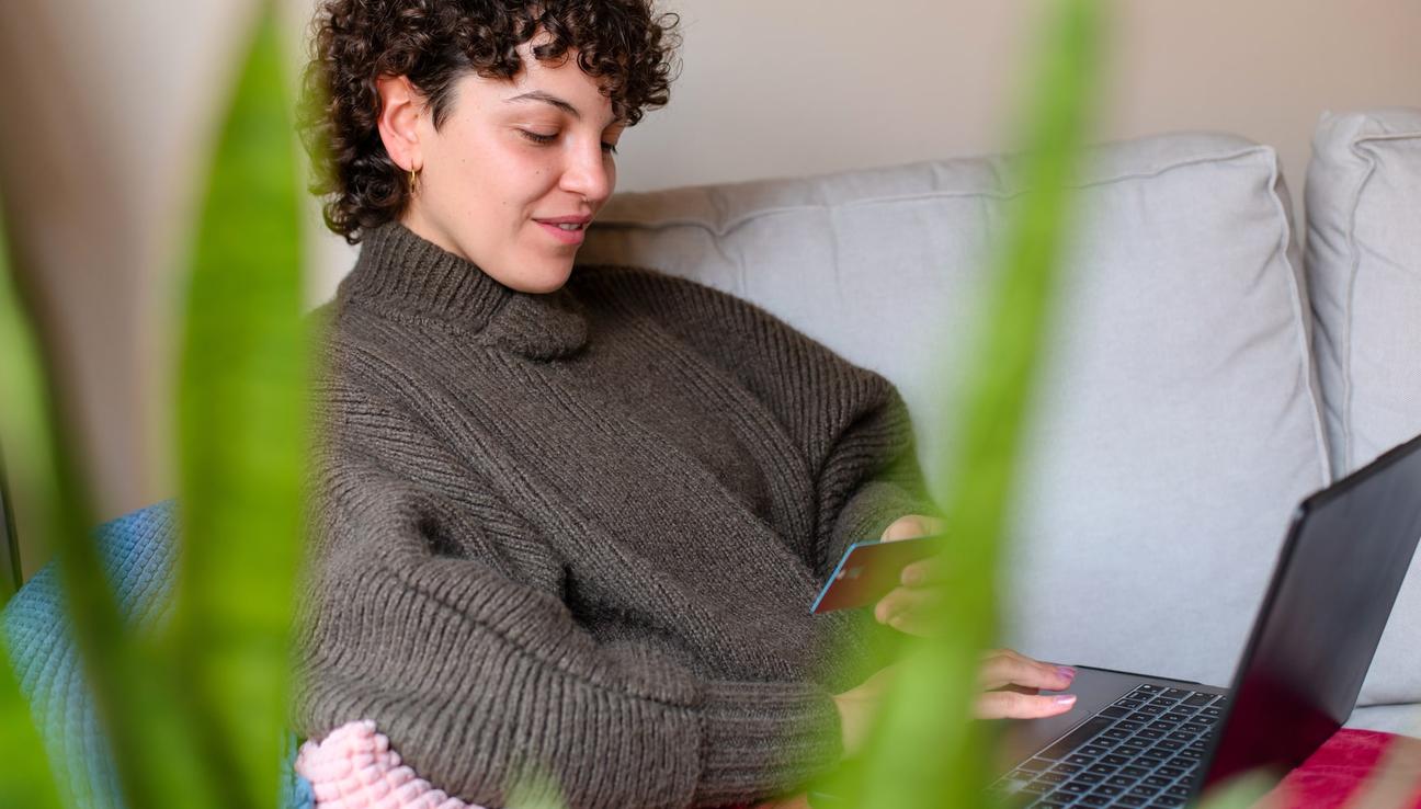 Kvinna med kreditkort i handen och laptop i knät