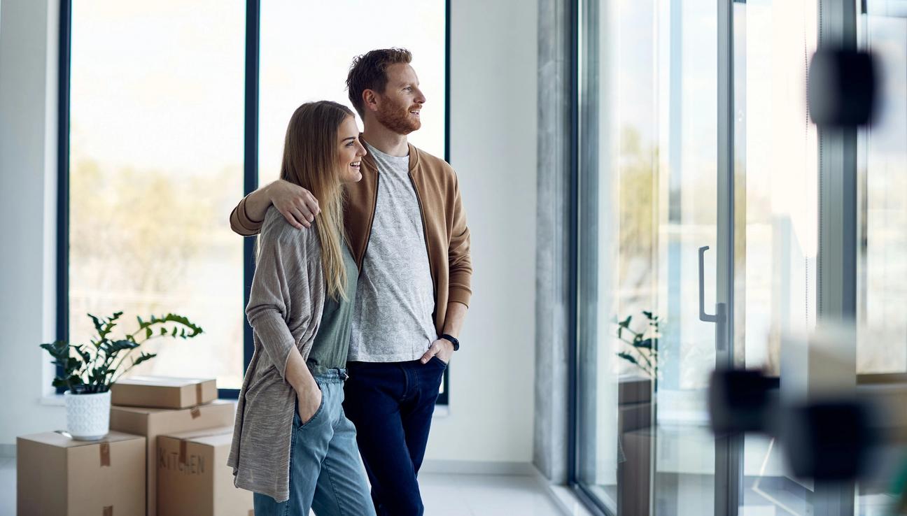 Ungt par har nettopp flyttet inn. De står sammen og ser ut gjennom glassveggen. bilde.