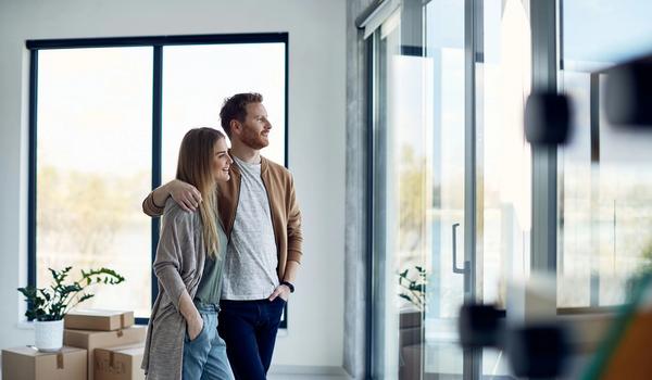 Ungt par har nettopp flyttet inn. De står sammen og ser ut gjennom glassveggen. bilde.