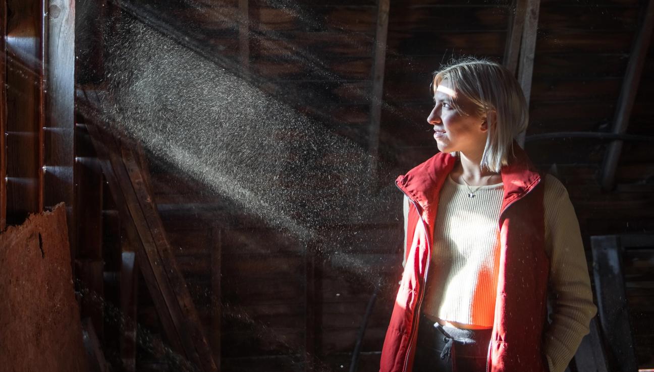 En kvinna som står i solljuset som sipprar igenom några sprickor på vinden