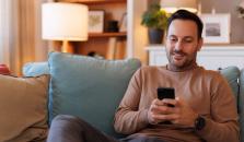 En mann sitter i sofaen og nettsurfer på mobilen sin. bilde.