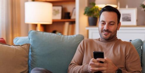 En mann sitter i sofaen og nettsurfer på mobilen sin. bilde.