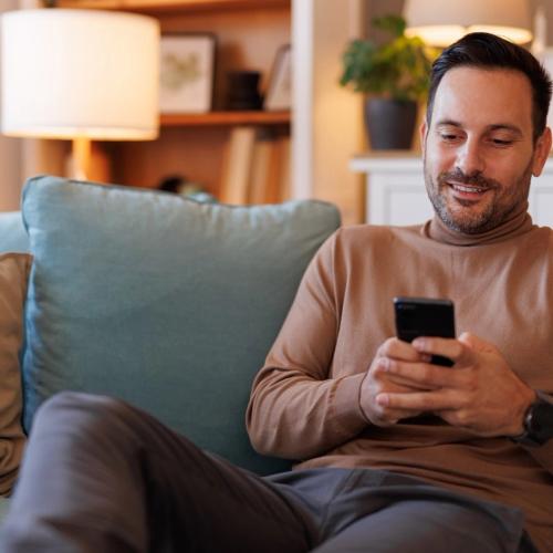 En mann sitter i sofaen og nettsurfer på mobilen sin. bilde.