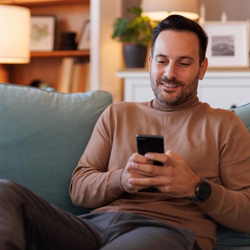 En mann sitter i sofaen og nettsurfer på mobilen sin. bilde.