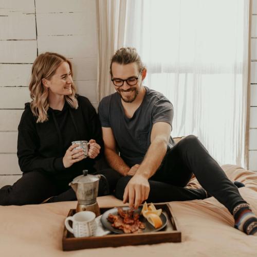 Ett par sitter på sängen och dricker kaffe, med en frukostbricka framför sig. foto.