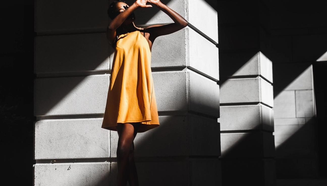 Kvinne i gul kjole holder opp hendene for sollyset. bilde.