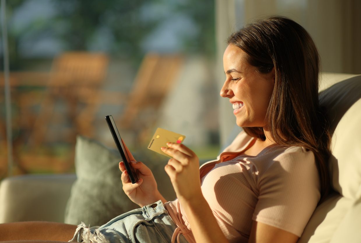 Dame sitter i sollyys med Morrow kredittkort i ene hånden og mobilen i den andre. bilde.