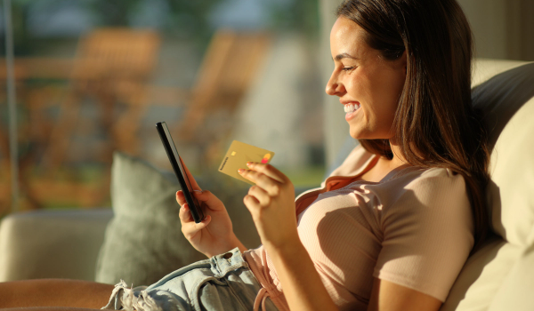 Dame sitter i sollyys med Morrow kredittkort i ene hånden og mobilen i den andre. bilde.