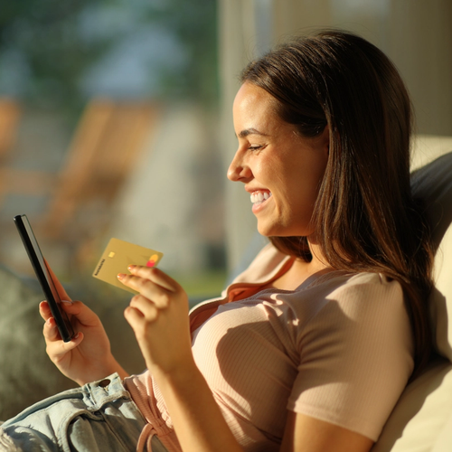 Dame sitter i sollyys med Morrow kredittkort i ene hånden og mobilen i den andre. bilde.