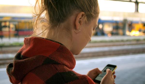 En jente me röd og svart rutete genser ser ned i mobilen. bilde.