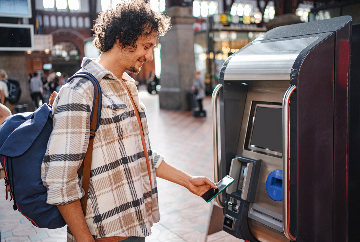 En mann kjøper togbillett og betaler med Morrow Bank kredittkort i mobilen. bilde,