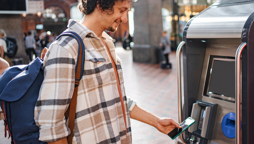 En mann kjøper togbillett og betaler med Morrow Bank kredittkort i mobilen. bilde,
