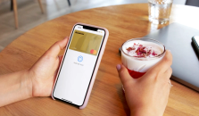 Hender som holder en mobil med Morrow digitalt gullkort og en drikke som er betalt med kortet. bilde.