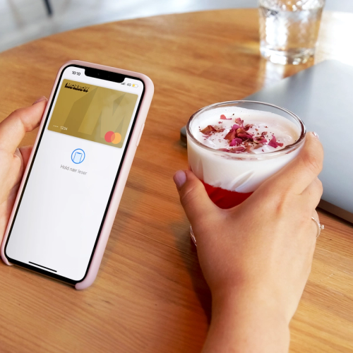 Hender som holder en mobil med Morrow digitalt gullkort og en drikke som er betalt med kortet. bilde.