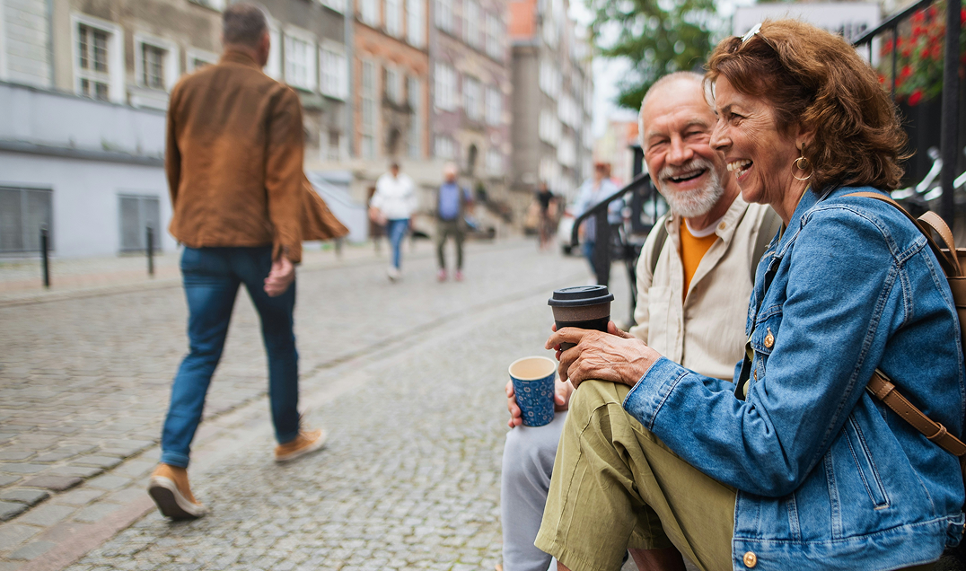 Seniori pariskunta juo kahvia kertakäyttömukeista ja istuu ulkoportailla.