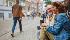 Seniori pariskunta juo kahvia kertakäyttömukeista ja istuu ulkoportailla.