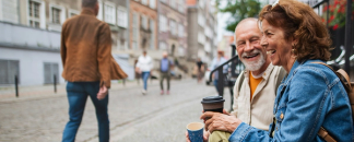 Seniori pariskunta juo kahvia kertakäyttömukeista ja istuu ulkoportailla.