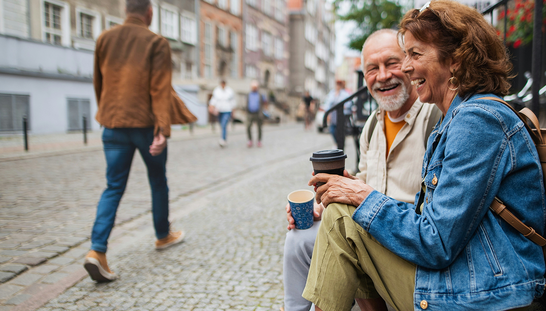 Seniori pariskunta juo kahvia kertakäyttömukeista ja istuu ulkoportailla.