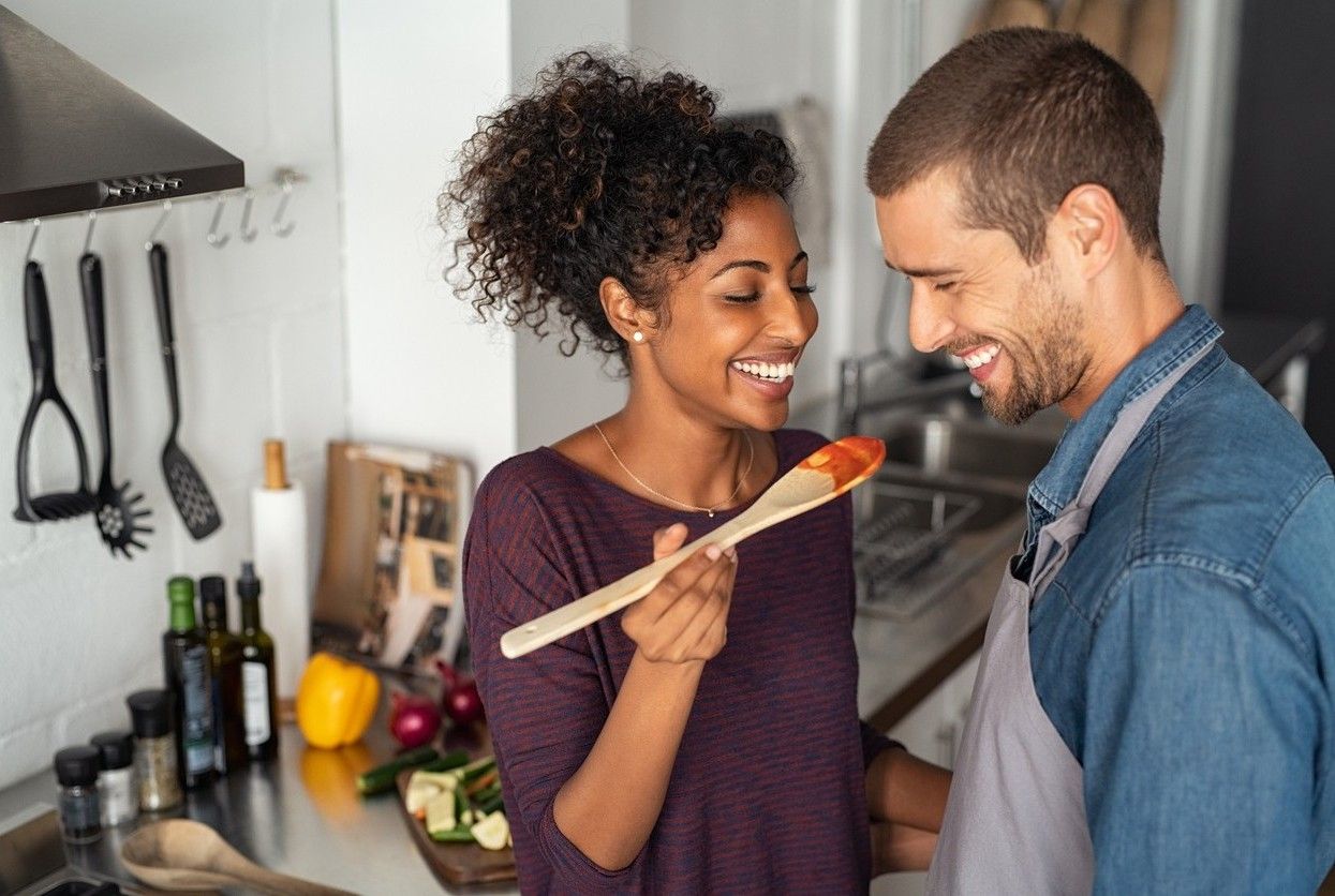 A man and woman cooking. The woman askes the man to taste. picture.