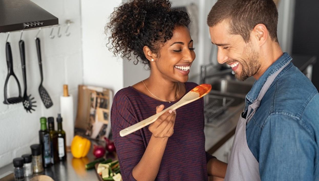 A man and woman cooking. The woman askes the man to taste. picture.