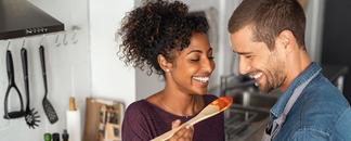 A man and woman cooking. The woman askes the man to taste. picture.