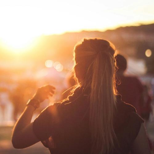 Jente med hestehale på festival i motlys. Mennesker beveger seg i bakgrunnen. Bilde.