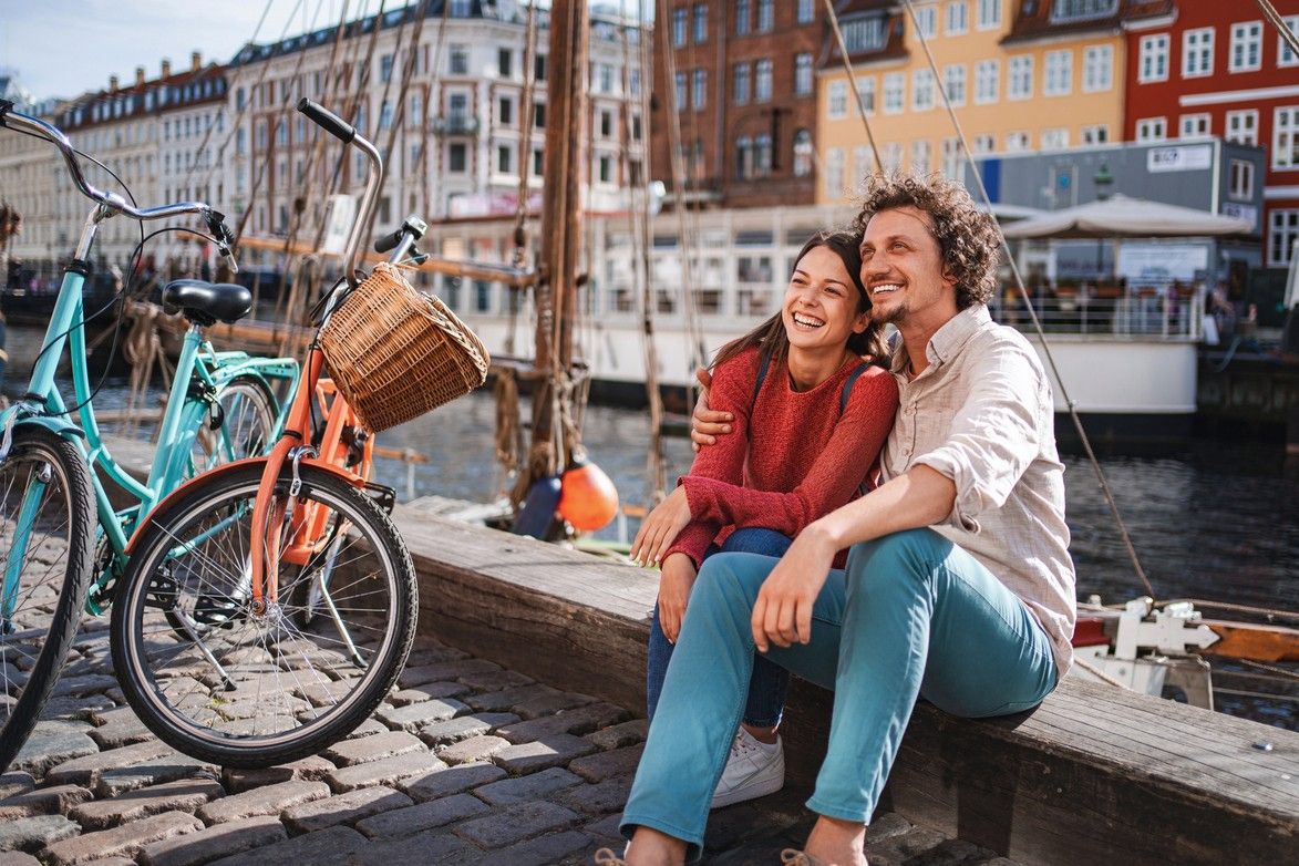 Ett par har parkerat cyklarna och satt sig i solen på kajkanten. foto.