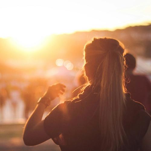 En kvinna på festival, på väg bort mot folkmängden i motljus. Foto.