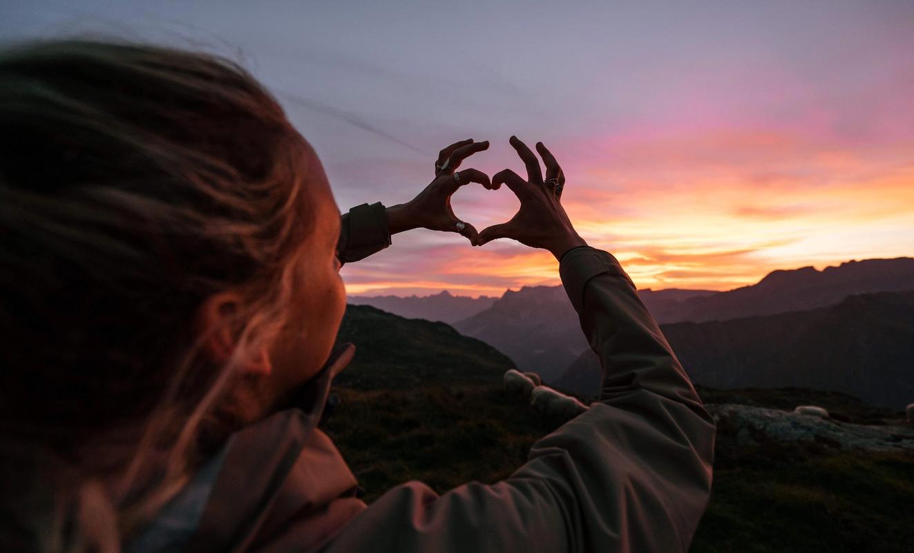 En kvinna gör ett hjärta med fingrarna och håller upp mot solnedgången