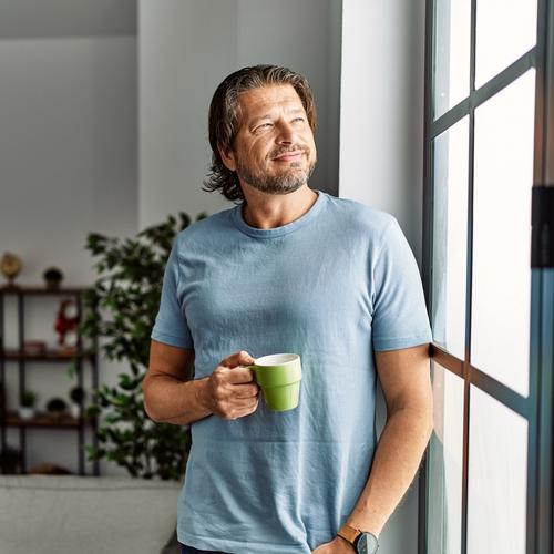 Man standing by the window with a cup of coffee in his hand. picture.