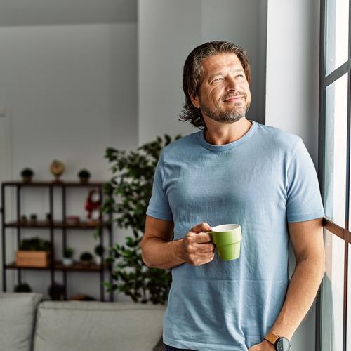 Man standing by the window with a cup of coffee in his hand. picture.