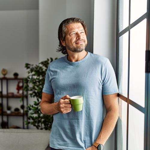 Man standing by the window with a cup of coffee in his hand. picture.