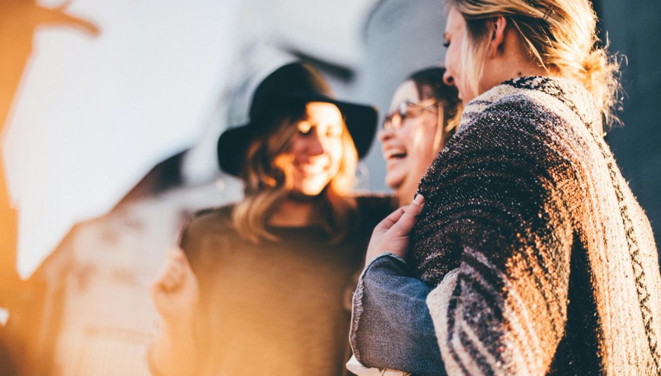 Iloiset naiset hymyilevät toisilleen auringonpaisteessa