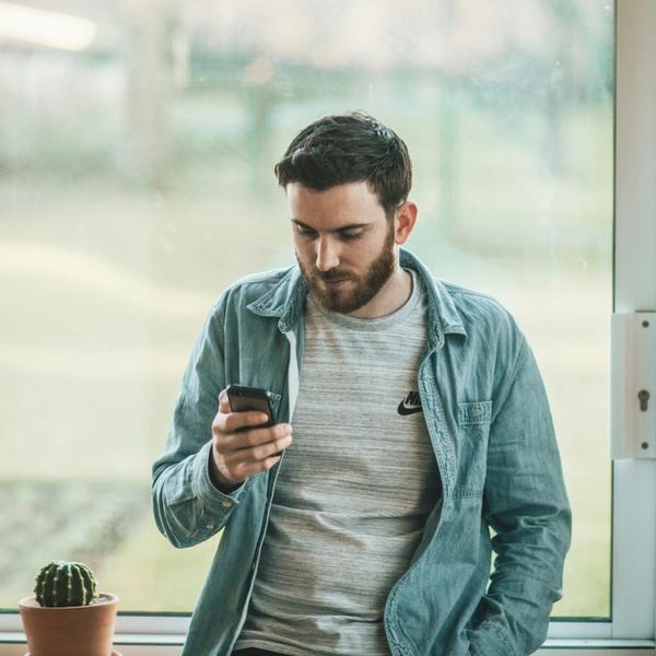Mann står ved vinduet og leser på telefonen. Han lurer på noe om sitt lån og trenger hjelp. bilde.