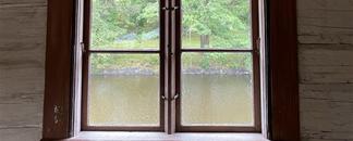 Vindu i gammel hytte, med takmalninger. Utenfor ser du vann og skogskant. bilde.