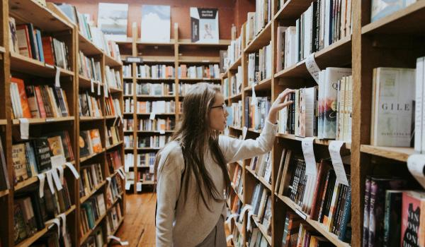 Jente går mellom hyllene på biblioteket og ser etter en bok. bilde