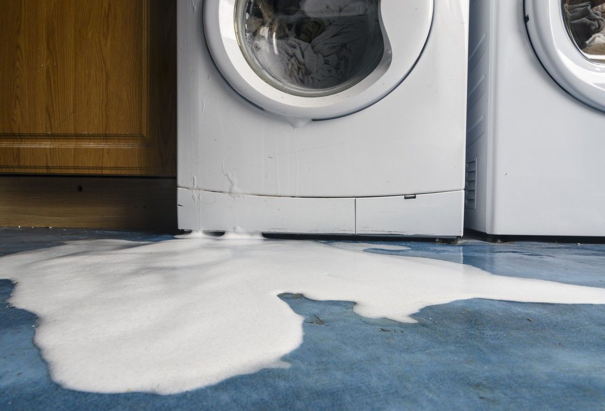 A washing machine that is broken, with water on the floor. picture.