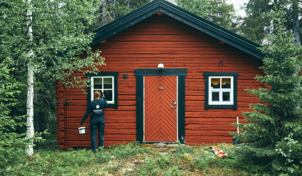 En kvinna målar fönstret på sin röda stuga