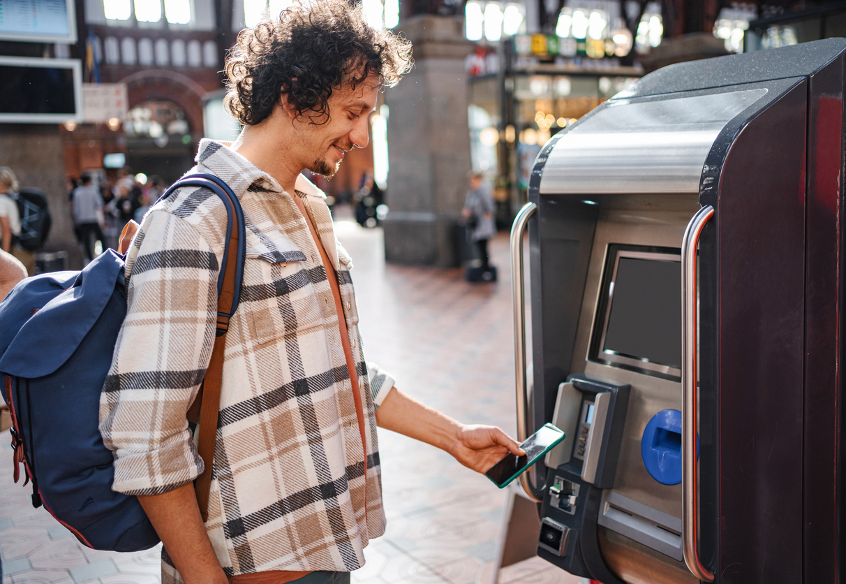 En man står på centralstationen och köper tågbiljett. Han betalar enkelt med Google pay i mobilen. foto.