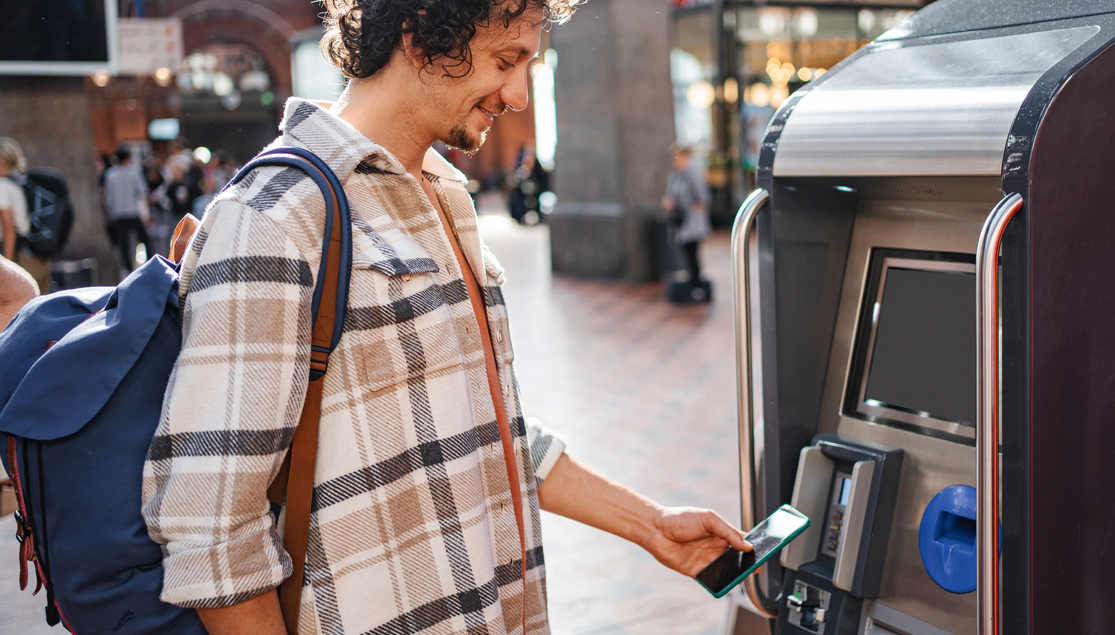 En man står på centralstationen och köper tågbiljett. Han betalar enkelt med Google pay i mobilen. foto.