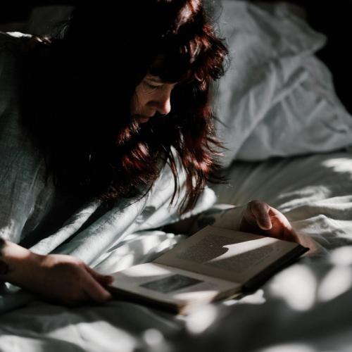 Kvinna ligger på sängen och läser en bok