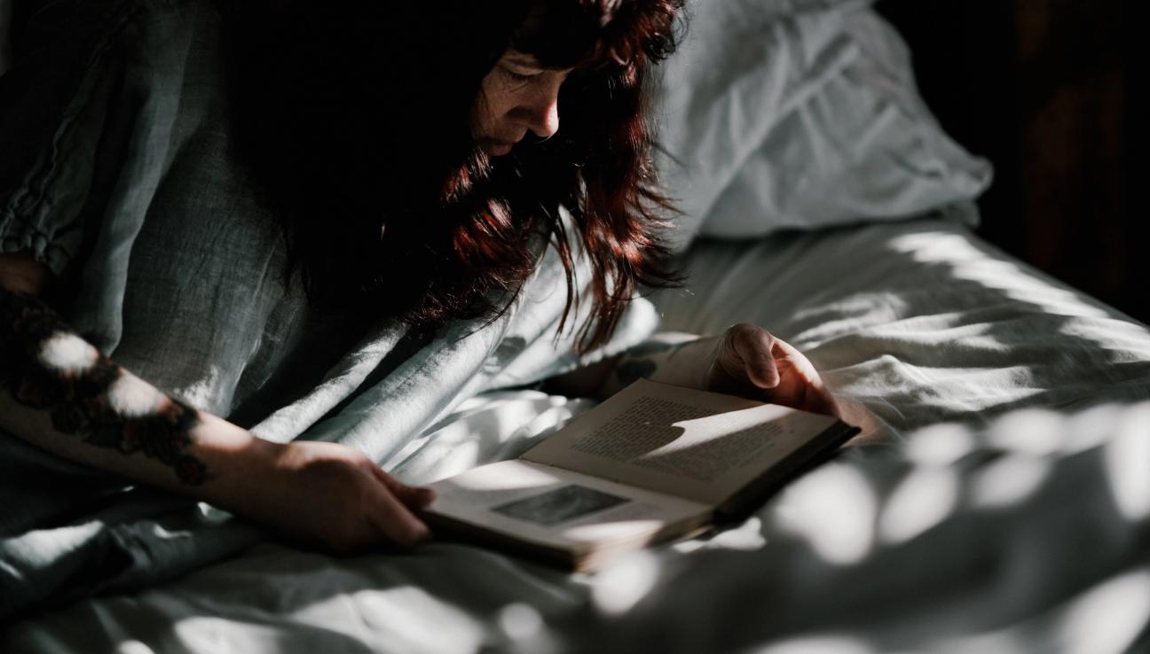 Kvinna ligger på sängen och läser en bok