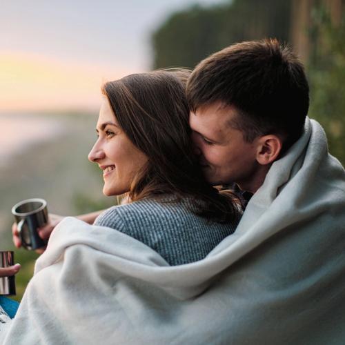 En mann og en dame står ute. Mannen har ett teppe om skuldrene som han også legger over damen. bilde.